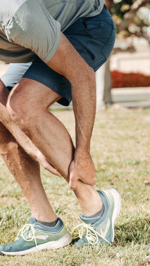 Adult male grabbing ankle due to injury in outdoor setting, wearing rubber running shoes.