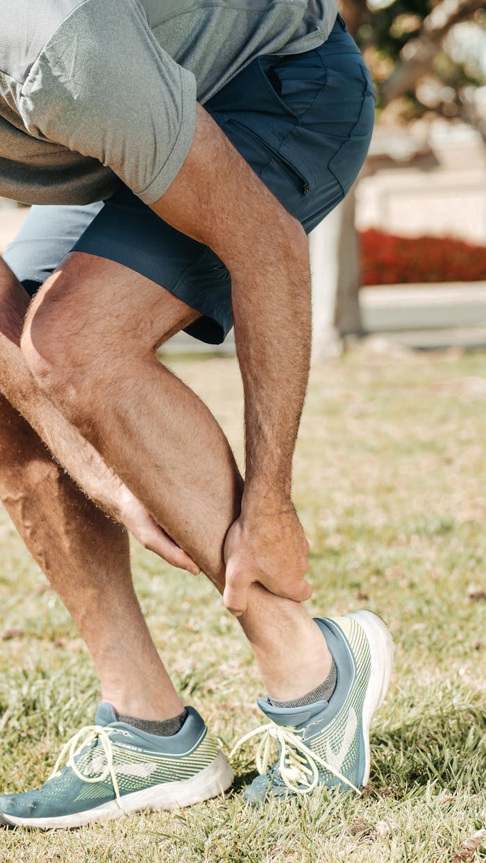 Adult male grabbing ankle due to injury in outdoor setting, wearing rubber running shoes.